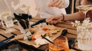 Daska sa sirevima, pršutom i maslinama uz čaše bijelog vina na stolu